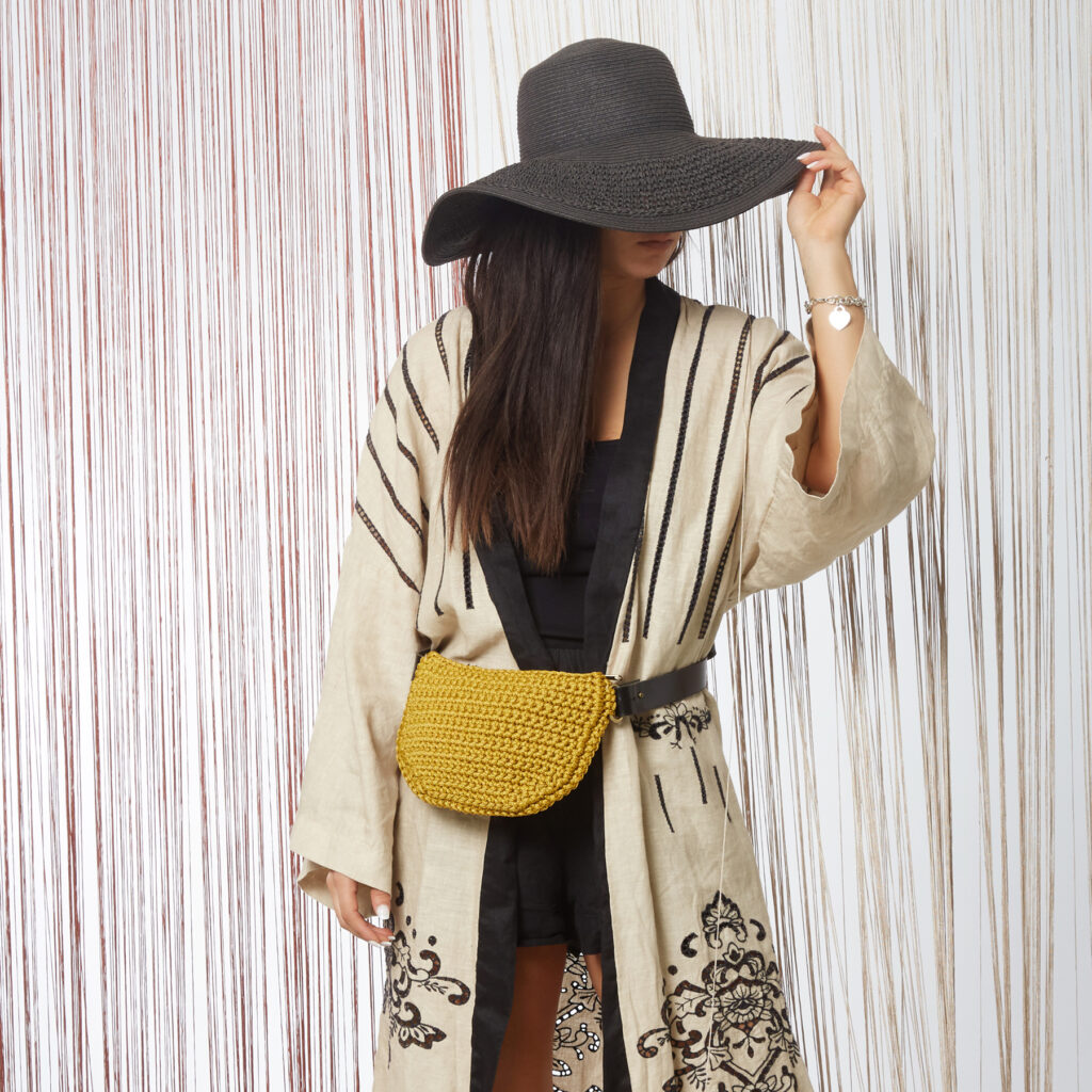 girl wears a handmade crochet belt bag in mustard color with black leather strap
