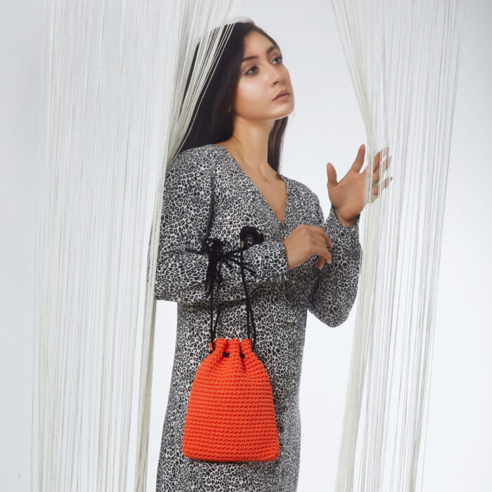 Girl holds in wrist a mini handmade crochet pouch bag in orange