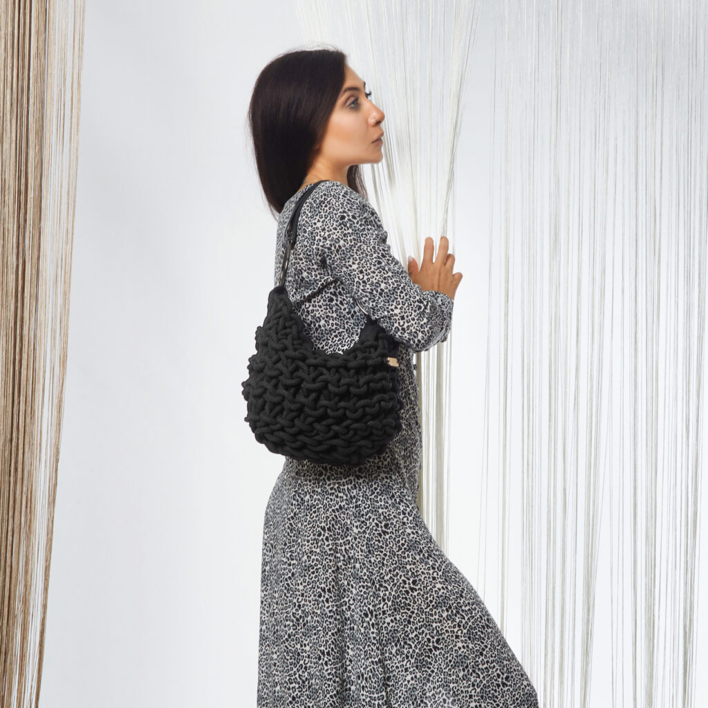 A girl holds a handmade knitted hobo bag with real leather adjustable strap, in black color