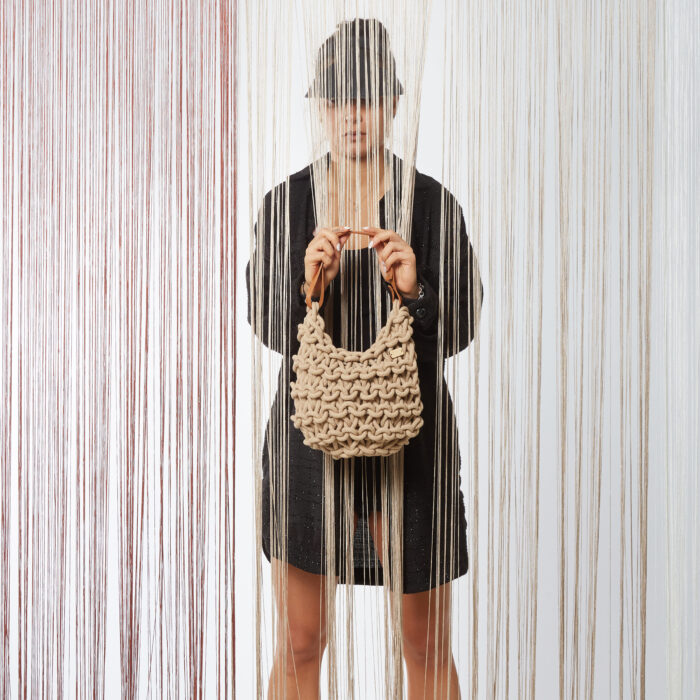 a girl holds a handmade knitted hobo shoulder bag with real leather adjustable strap, in beige color